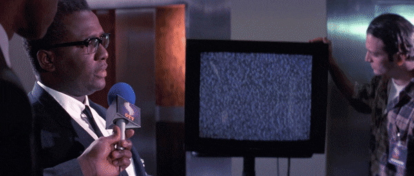 Animated GIF of scene from Hackers (1995), FBI agent is giving a news interview when a television in background is interrupted by static and the smiling face of the hacker character Cereal Killer appears saying "Hola, boys and girls!"