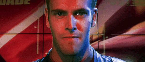 GIF of scene from Hackers (1995) film. The face of character Dade Murphy closeup, focused on playing a video game, contorting face, biting lip, as visual of the Wipeout racing game on a large screen spins and flashes in background. His player name DADE and score in neon yellow in top corners.