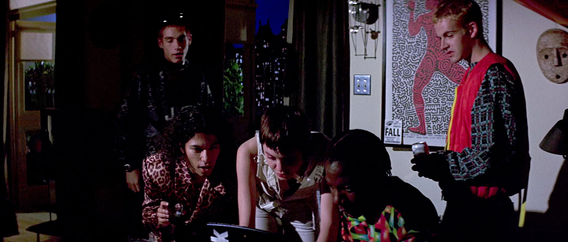 Scene from Hackers (1995) film with the characters Kate Acid Burn, Phantom Phreak, Lord Nikon and Dade Crash Override gathered around a laptop in Kate's darkened bedroom. Kate's boyfriend Curtis appearing behind them annoyed at the distraction, 'Kate, you're not going into that computer shit now, right?'