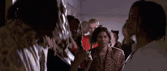 Animated GIF of scene from Hackers (1995) of characters Phantom Phreak and Dade Murphy walking into a house party breaking a crowd of partygoers gathered and smoking in a hallway. Phreak strutting in between them in a leopard-print shirt and jacket. Dade following behind in bight red vest jacket.