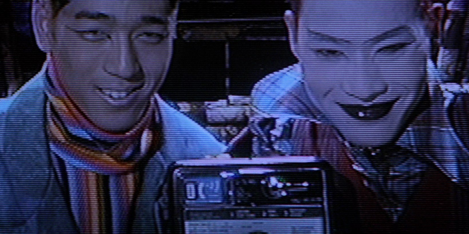 Scene from Hackers (1995) film featuring characters Razor and Blade in colorful fashion attire on their pirate tv show with amateur video grain quality, smiling behind a payphone as they demonstrate phone phreaking hacker techniques. 'That's right, this is a payphone... Don't ask!', they exclaim.