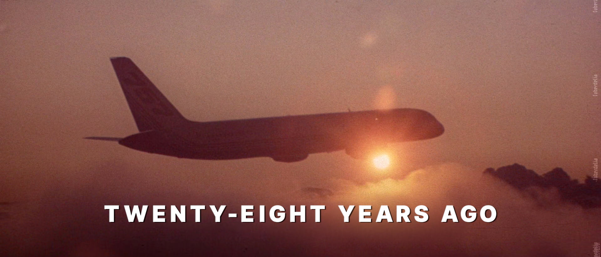 Screencap of opening scene from Hackers (1995) of an airplane flying above clouds, mostly silhouetted as the sun shines a bright orange, peeking, beaming from behind the plane. Large white sans-serif text below the plain caption says: TWENTY-EIGHT YEARS AGO.