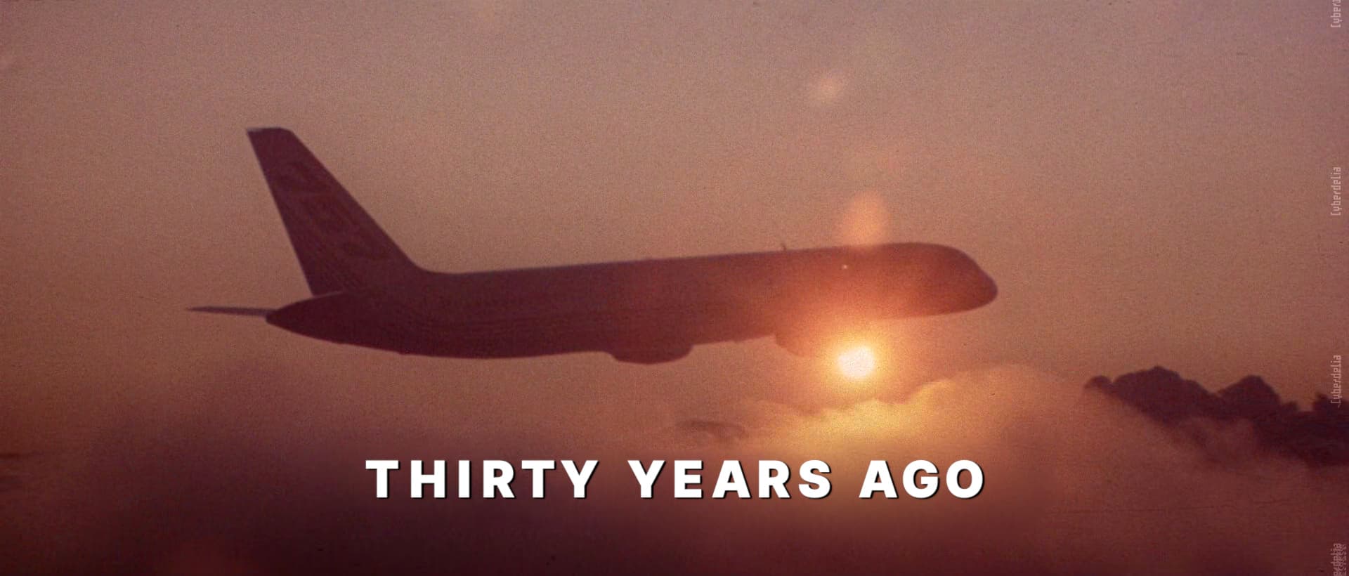 Screencap of opening scene from Hackers (1995) of an airplane flying above clouds, mostly silhouetted as the sun shines a bright orange, peeking, beaming from behind the plane. Large white sans-serif text below the plain caption says: THIRTY YEARS AGO. Edit by Cyberdelia NYC.