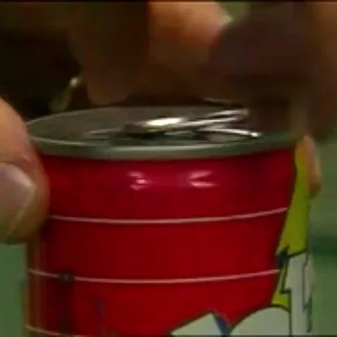 Animated GIF of video clips of a hand close up opening a can of Jolt Cola, flipping the tab, then another from a different angle, then a scene of the top of can tilted, pouring as dark brown soda stream pours out slowly for a few seconds.